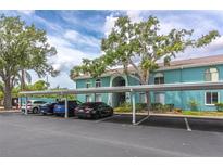 Exterior of condo building with covered parking, teal paint, landscaping, and white trim against a partially cloudy blue sky at 11404 2Nd N St # 3, St Petersburg, FL 33701