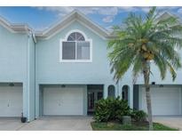 Inviting light blue two-story townhome with white garage doors, palm tree, and lush landscaping at 623 Garland Cir, Indian Rocks Beach, FL 33785