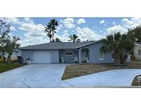 Charming single-story home with a wide driveway, an attached garage, and palm trees on a partially sunny day at 10208 Oak Hill Dr, Port Richey, FL 34668