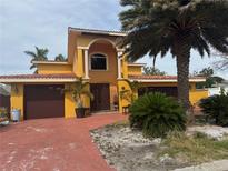 Two-story stucco home with a red driveway, arched entry, two-car garage, and lush landscaping at 11105 8Th E St, Treasure Island, FL 33706