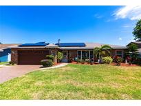Charming brick home featuring solar panels, a well-manicured lawn, and vibrant landscaping at 2188 Kent Ave, Clearwater, FL 33764