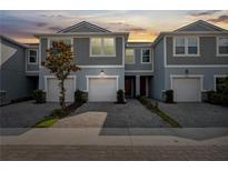 Charming townhome with gray siding, a one-car garage, and a well-maintained paver driveway under a sunset sky at 2529 Arbor Wind Dr, Lutz, FL 33558