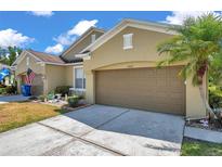 Tan home featuring a brown garage door, palm tree, well manicured lawn and a sunny sky at 30327 Lettingwell Cir, Wesley Chapel, FL 33543