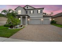 Charming two-story home featuring a three-car garage, brick paved driveway, and tropical landscaping at sunset at 13311 Orca Sound Dr, Riverview, FL 33579