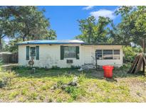 Exterior view of single story white home with green shutters and blue tarp roof surrounded by unkempt yard at 4815 N Falkenburg Rd, Tampa, FL 33610