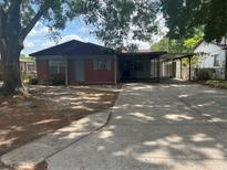Charming single story home with red brick and grey siding, a covered driveway and mature trees in the yard at 7401 N Albany Ave, Tampa, FL 33604