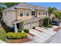 Two-story tan townhome featuring an attached garage, lush landscaping, and a driveway for convenient parking at 1051 Andrew Aviles Cir, Tampa, FL 33619