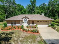 Charming single-story home featuring a manicured lawn, mature trees, and a welcoming two-car garage at 11120 Lu Wista Ln, Brooksville, FL 34601
