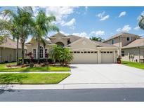 Beautiful home featuring a large driveway, three-car garage, and lush landscaping with palm trees at 3300 Stonegate Falls Dr, Land O Lakes, FL 34638