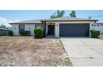 Charming single-story home featuring a well-maintained lawn and a dark gray garage door at 12456 Spreading Oak Dr, Spring Hill, FL 34609