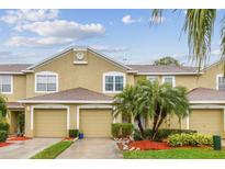 Townhouse featuring attached garage, neutral toned stucco exterior, and tidy landscaping with palm trees at 11162 Kapok Grand Cir, Madeira Beach, FL 33708