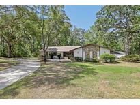 Charming ranch-style home featuring a stone facade and a lush, green front lawn surrounded by mature trees at 1221 Candlelight Blvd, Brooksville, FL 34601
