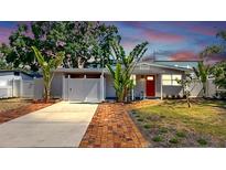 Charming one-story home with a red door, well-manicured lawn, tropical landscaping, and driveway at 4735 W Oklahoma Ave, Tampa, FL 33616