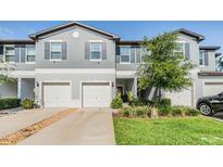 Charming townhome featuring a gray exterior, white garage doors, and well-maintained landscaping at 1594 Cassius St, Lutz, FL 33549