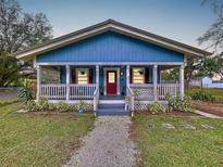 Charming blue home featuring a welcoming covered porch, red door, and freshly landscaped yard at 3213 E Genesee St, Tampa, FL 33610