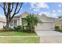 Charming home featuring a two-car garage, beautifully landscaped yard with palm trees, and neutral exterior paint at 5628 Terrain De Golf Dr, Lutz, FL 33558