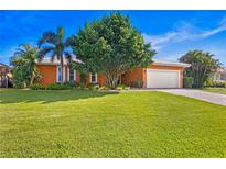Well-maintained house featuring an orange facade, lush green lawn, a two car garage, and mature trees at 1960 Montana Ne Ave, St Petersburg, FL 33703