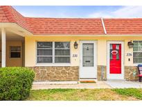 Charming condo featuring a decorative stone facade, bright red roof, and well-manicured landscaping at 230 Portree Dr, Dunedin, FL 34698