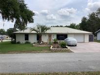 Charming single-story home with a metal roof, a well-manicured lawn, and a covered car in the driveway at 6488 Robinswood Ave, Brooksville, FL 34602