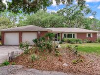 Charming brick home with a two-car garage and beautifully landscaped front yard filled with flowers and mature trees at 7216 N Mobley Rd, Odessa, FL 33556