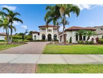 Stately two-story home featuring a red tile roof, balconies, and a lushly landscaped yard with mature palm trees at 16406 Chapman Crossing Dr, Lithia, FL 33547
