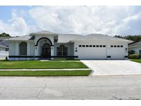 Inviting white home featuring a well-manicured lawn and a three-car garage at 1961 Dunbrody Ct, Dunedin, FL 34698