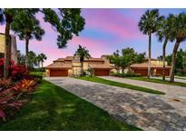 Beautiful sunset view of the home exterior featuring a patterned brick driveway and lush landscaping with palm trees at 2421 Lake Point Ln, Clearwater, FL 33762