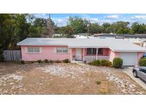 Charming, sun-drenched single story home featuring pink facade, white trim, covered porch, and drought resistant landscaping at 3317 Nakora Dr, Tampa, FL 33618