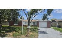 Charming single-story home with a brick facade, attached garage, and front yard with mature trees at 6105 Westport Dr, Port Richey, FL 34668