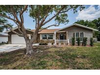 Charming single-story home with stone facade, well-manicured lawn, and mature shade tree at 1402 Oleander Dr, Tarpon Springs, FL 34689