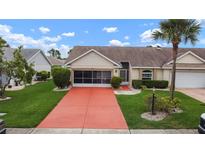 Charming single-story home featuring a well-manicured lawn, tidy landscaping, and a bright red driveway at 2015 W Del Webb Blvd, Sun City Center, FL 33573