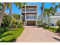 Stunning two-story home with a brick driveway and beautiful landscaping with palm trees against a clear blue sky at 443 18Th Ave, Indian Rocks Beach, FL 33785