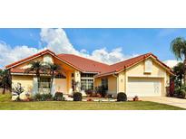 Charming yellow home featuring a red tile roof, well-manicured lawn, tropical landscaping, and an attached two-car garage at 5001 Queen Palm Ne Ter, St Petersburg, FL 33703
