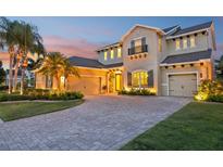 Elegant two-story home with a paver driveway, lush landscaping, and a welcoming entrance at dusk at 11327 Lake Lucaya Dr, Riverview, FL 33579