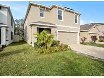 Inviting two-story home featuring manicured lawn, lovely landscaping, and an attached two-car garage at 17012 Oval Rum Dr, Wimauma, FL 33598