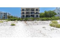 Beachfront building with multiple balconies overlooks a pristine white sand beach with lush vegetation at 3200 Gulf Blvd # 202, St Pete Beach, FL 33706
