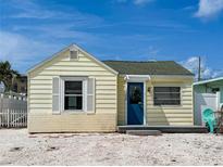 Charming cottage-style home features a bright yellow exterior and a quaint blue front door, creating a welcoming facade at 13326 1St E St, Madeira Beach, FL 33708