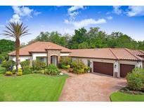 Beautiful single-story home featuring a clay tile roof, lush landscaping, and a brick paved driveway at 14910 Tom Fazio Ct, Tampa, FL 33626