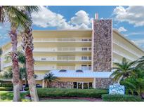 Multi-story building with stone facade and balconies surrounded by lush tropical landscaping with palm trees at 2504 Gulf Blvd # 201, Indian Rocks Beach, FL 33785