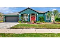 Charming home exterior with teal paint, a red front door, landscaping, and a two-car garage at 5103 Rushbrook Rd, Land O Lakes, FL 34638