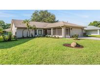Single-story home with a well-manicured front yard, mature landscaping, and a screened entryway at 3956 Tarpon Pointe Cir, Palm Harbor, FL 34684