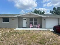 Charming single-story home featuring a well-manicured lawn and a cozy front porch with pink Adirondack chairs at 7525 Arbordale Dr, Port Richey, FL 34668