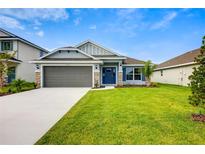 Charming single-story home with a manicured lawn, gray garage door, and blue front door at 16511 66Th E Ln, Parrish, FL 34219