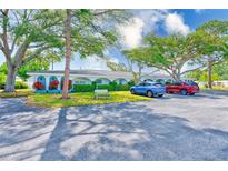 Exterior shot of the condo, featuring trees, lush landscaping, and a parking area with two cars at 11200 102Nd Ave # 75, Seminole, FL 33778
