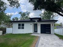 Beautiful single Gathering home with a white exterior, black trim, a modern garage door, and manicured lawn at 12308 Pittsfield Ave, Tampa, FL 33624