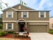 Two-story home featuring neutral stucco, white trim, shuttered windows, a two car garage, and a landscaped front yard at 12607 Flatwood Creek Dr, Riverview, FL 33578