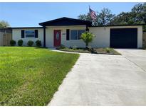 Charming one story home with large front yard, colorful door, dark shutters and an American flag at 12907 College Hill Dr, Hudson, FL 34667