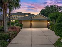 Two-car garage with stone accents, mature landscaping, and a wide driveway under a stunning dusk sky at 13209 Palmilla Cir, Dade City, FL 33525