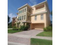 Three-story townhome featuring a two-car garage, neutral stucco exterior, and brick paver driveway at 1532 Citrine Trl, Tarpon Springs, FL 34689