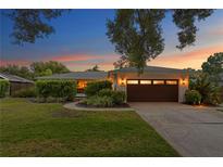 Beautiful single-story home featuring a two-car garage, lush landscaping, and a well-manicured lawn at sunset at 2665 Clubhouse N Dr, Clearwater, FL 33761